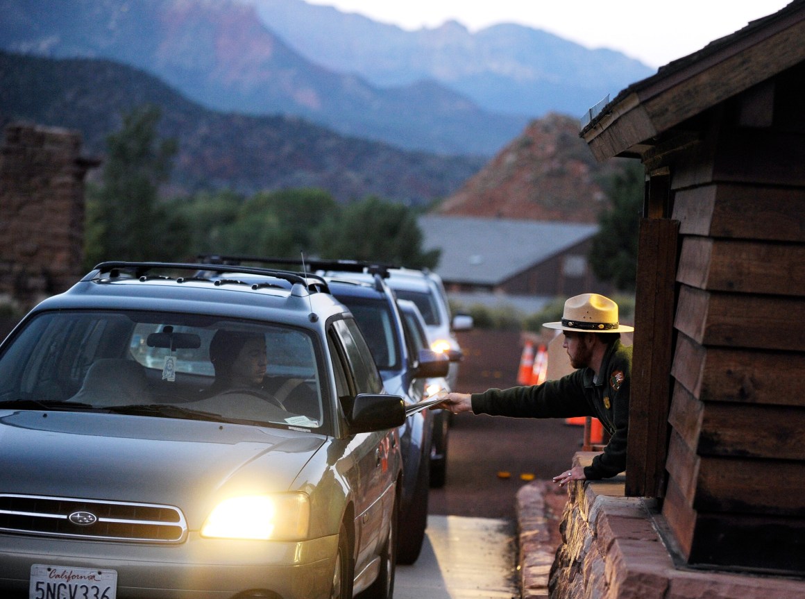 A park ranger Lee Wilson (R) passes out park information to visitors at the entrance to Zion National Park in Springdale, Utah.