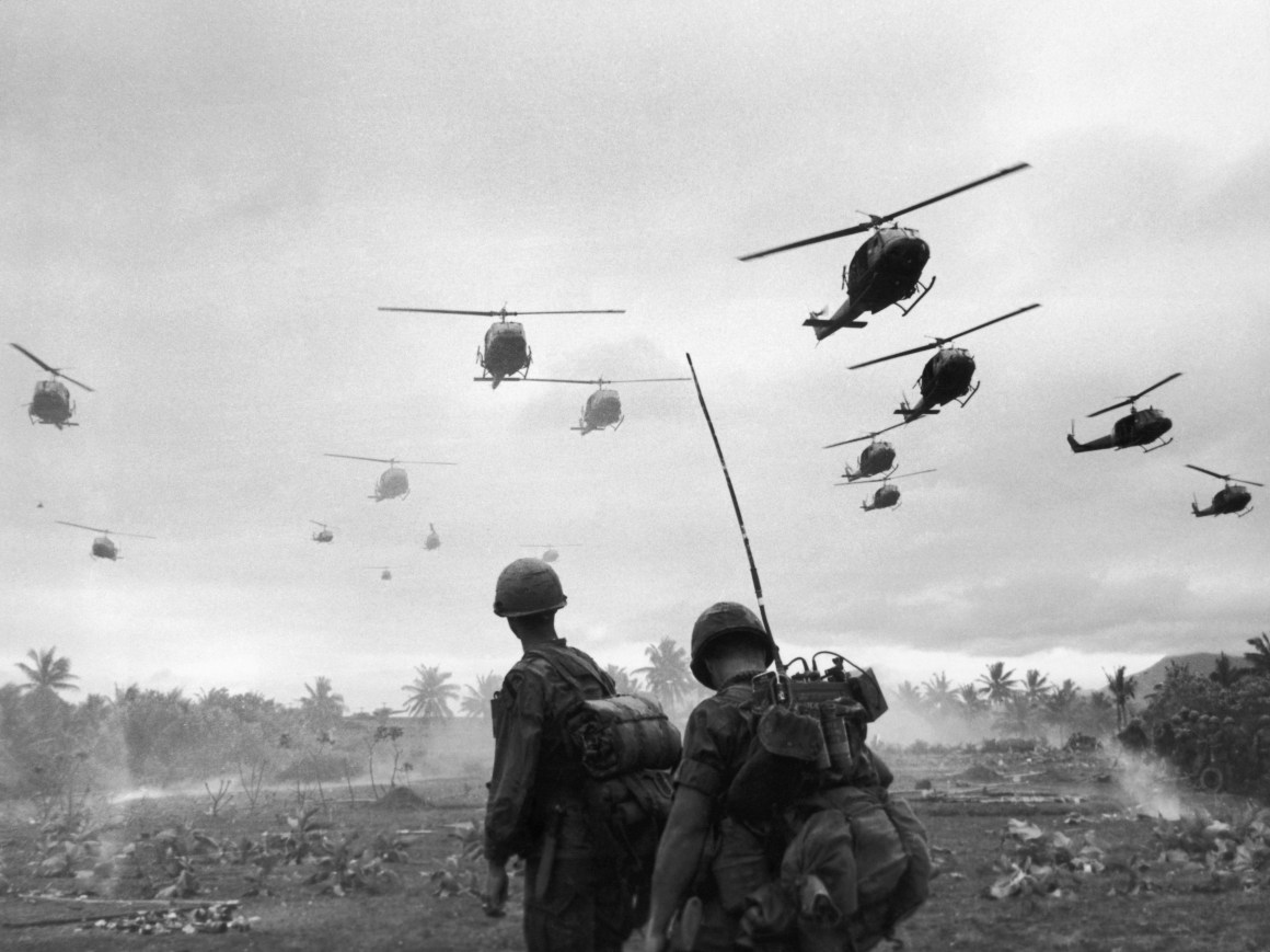 The second wave of combat helicopters of the 1st Air Cavalry Division fly over an RTO and his commander on an isolated landing zone during Operation Pershing, a search and destroy mission on the Bong Son Plain and An Lao Valley of South Vietnam, during the Vietnam War.