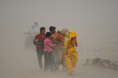 Indian Hindu devotees walk through a dust storm at the Sangam.