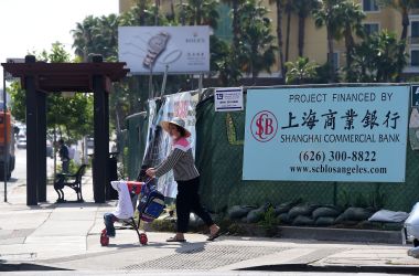 A woman pushes a stroller in San Gabriel, California, on May 17th, 2016, past a banner at a construction site project financed by the Shanghai Commercial Bank.