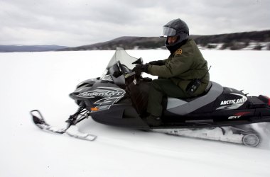 A U.S. Border Patrol Agent rides a snowmobile during a patrol on a frozen lake that splits the Canadian territory behind him and the U.S., near Norton, Vermont.