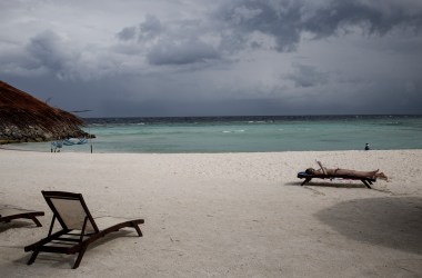 Tourists relax on the beach with rain on the horizon on in Maafushi, Maldives. A new study attributes the vast majority of the Maldives' emissions to tourism.