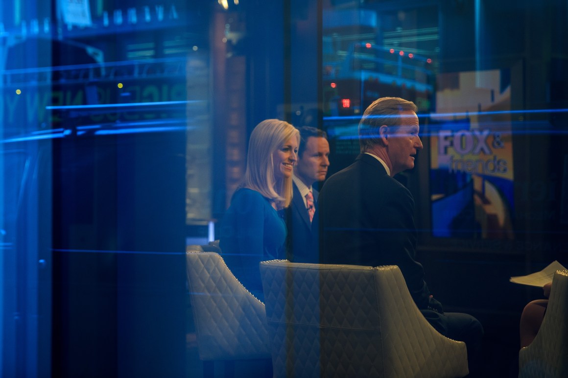 Seen through a window, (from left) hosts Ainsley Earhardt, Brian Kilmeade, and Steve Doocy broadcast Fox and Friends from the Fox News studios on February 17th, 2017, in New York City.