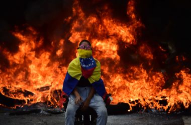 A Venezuelan opposition activist is backdropped by a burning barricade during a demonstration against President Nicolas Maduro in Caracas, on April 24th, 2017. Protesters rallied on Monday vowing to block Venezuela's main roads to raise pressure on Maduro after three weeks of deadly unrest that have left 21 people dead. Riot police fired rubber bullets and tear gas to break up one of the first rallies in eastern Caracas early Monday while other groups were gathering elsewhere, the opposition said.