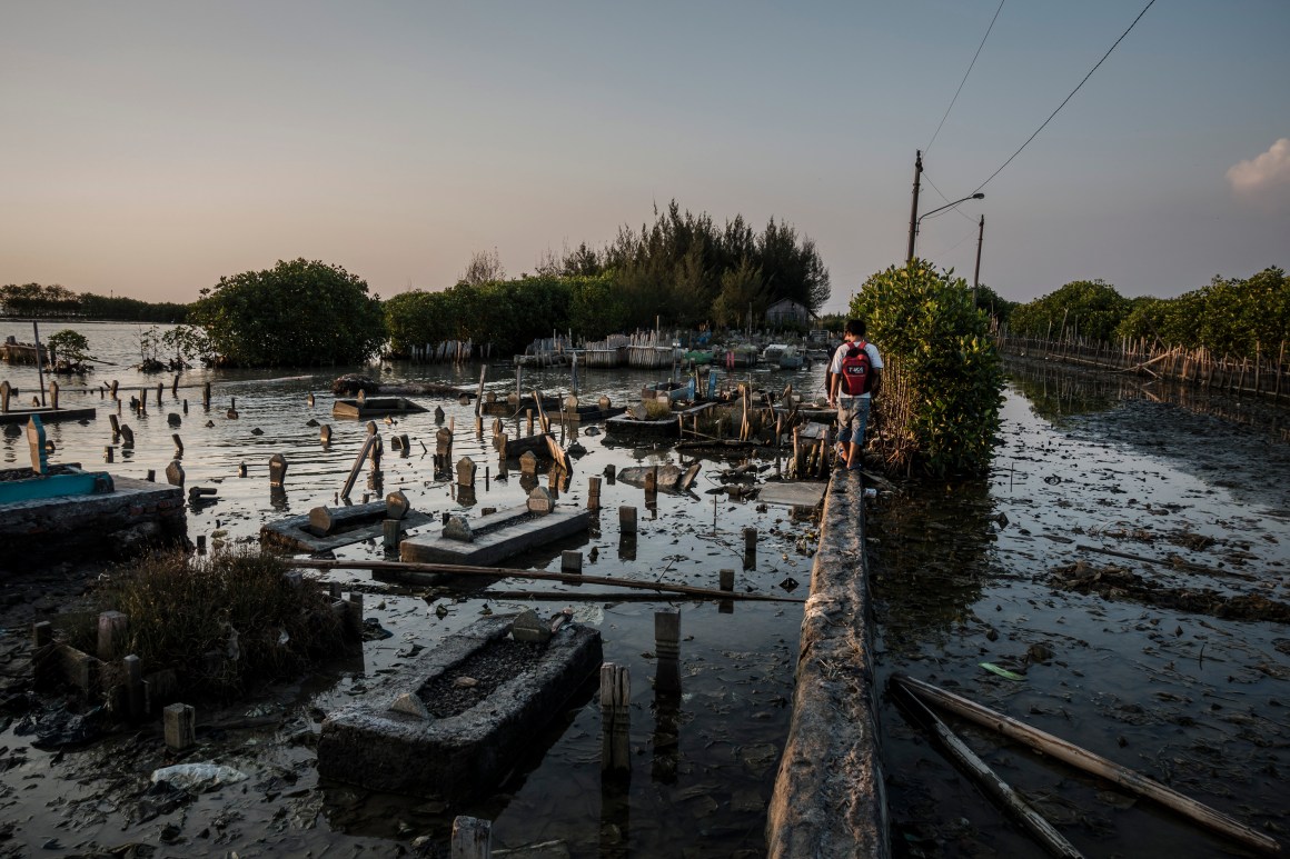 A man walks through a public cemetery submerged by flood waters from rising sea levels on June 8th, 2017, in Semarang, Indonesia.