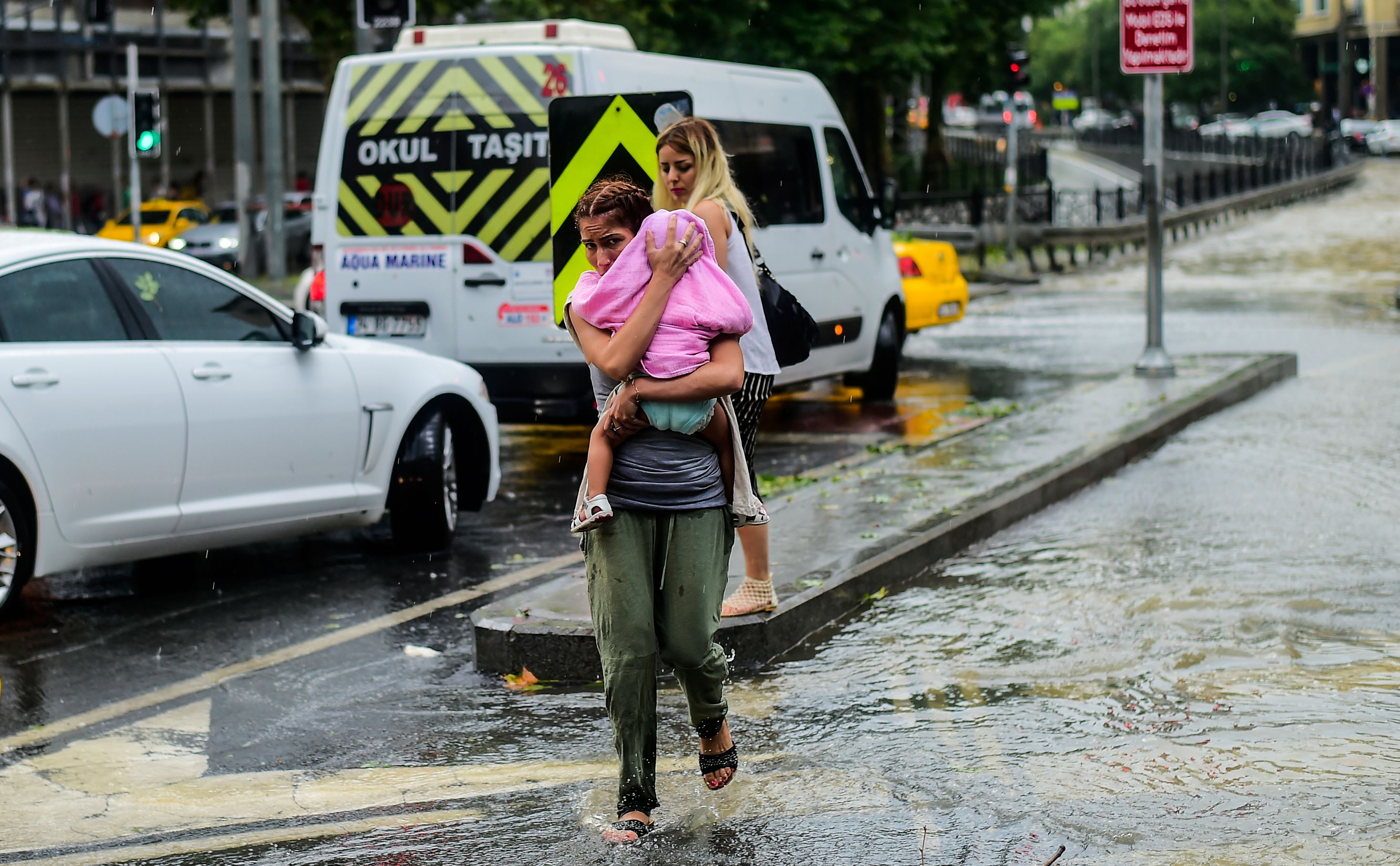 A woman carrying a baby crosses a street during a heavy downpour of rain at Taksim in Istanbul on July 27th, 2017.