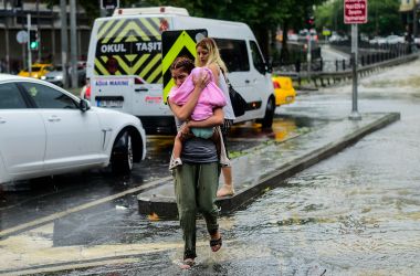 A woman carrying a baby crosses a street during a heavy downpour of rain at Taksim in Istanbul on July 27th, 2017.