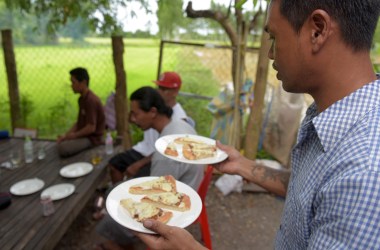 Nheb Thai, a Cambodian refugee who was deported from the U.S., carries plates with pizza as he serves a meal to a group of other deportees in Cambodia.