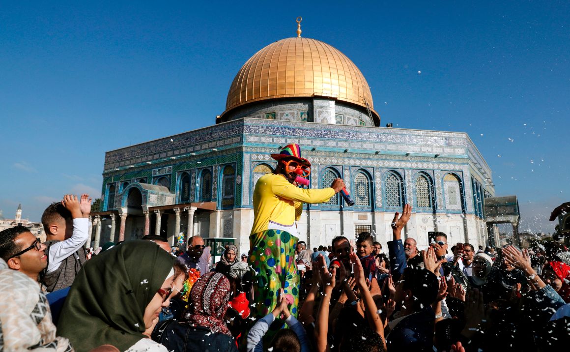 A man dressed in a clown outfit distributes balloons to children as confetti is thrown by the Dome of the Rock inside al-Aqsa Mosque compound, in Jerusalem's old city on the first day of Eid al-Adha on September 1st, 2017.