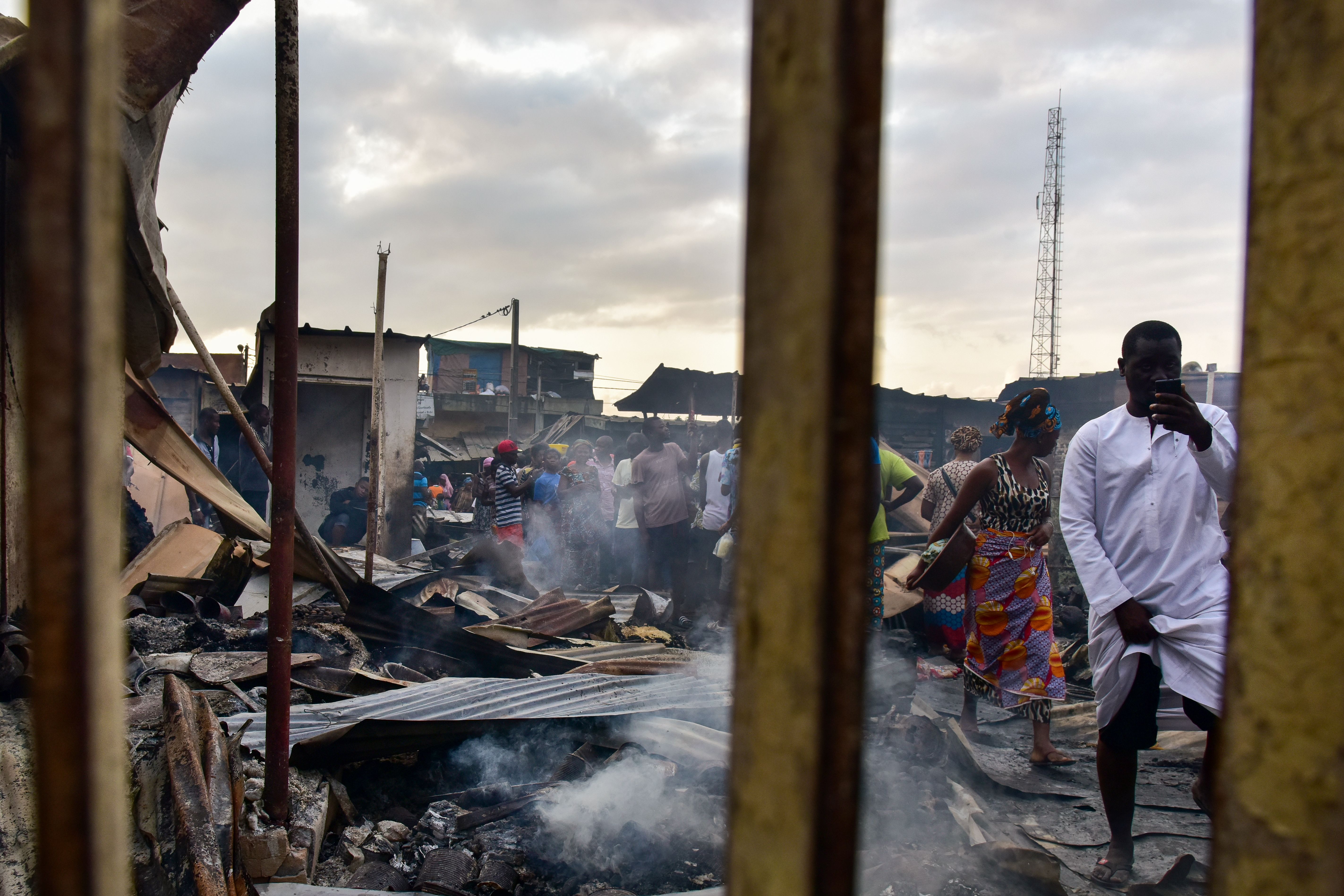 A man takes photos with a mobile phone as sellers walk through debris in a market after a fire devastated the building overnight on September 18th, 2017, in the Abobo neighborhood of Abidjan.