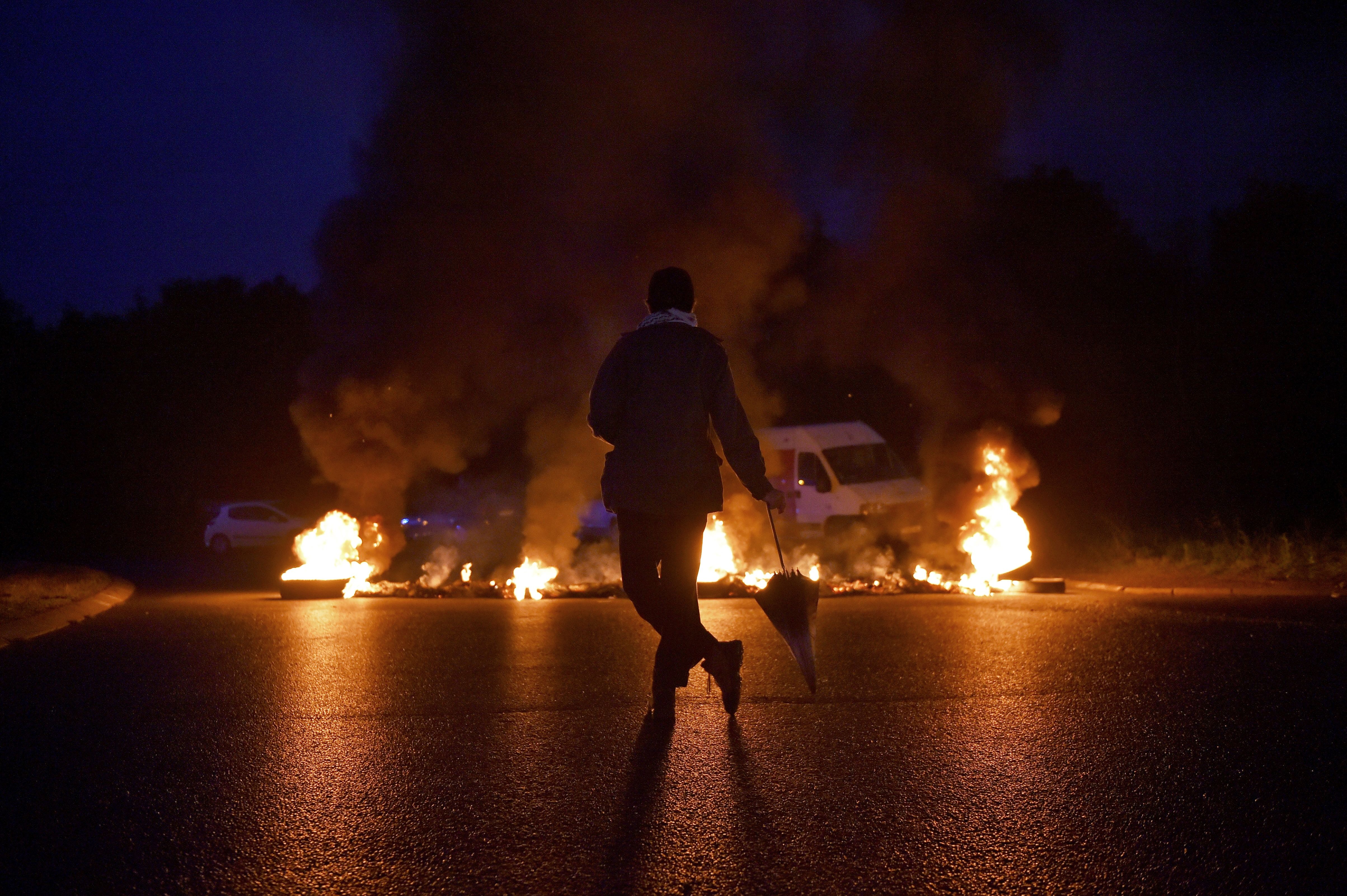 A protester watches a burning traffic circle while union trade members block trucks on September 25th, 2017, in Donges, France, to protest the government's labor law.