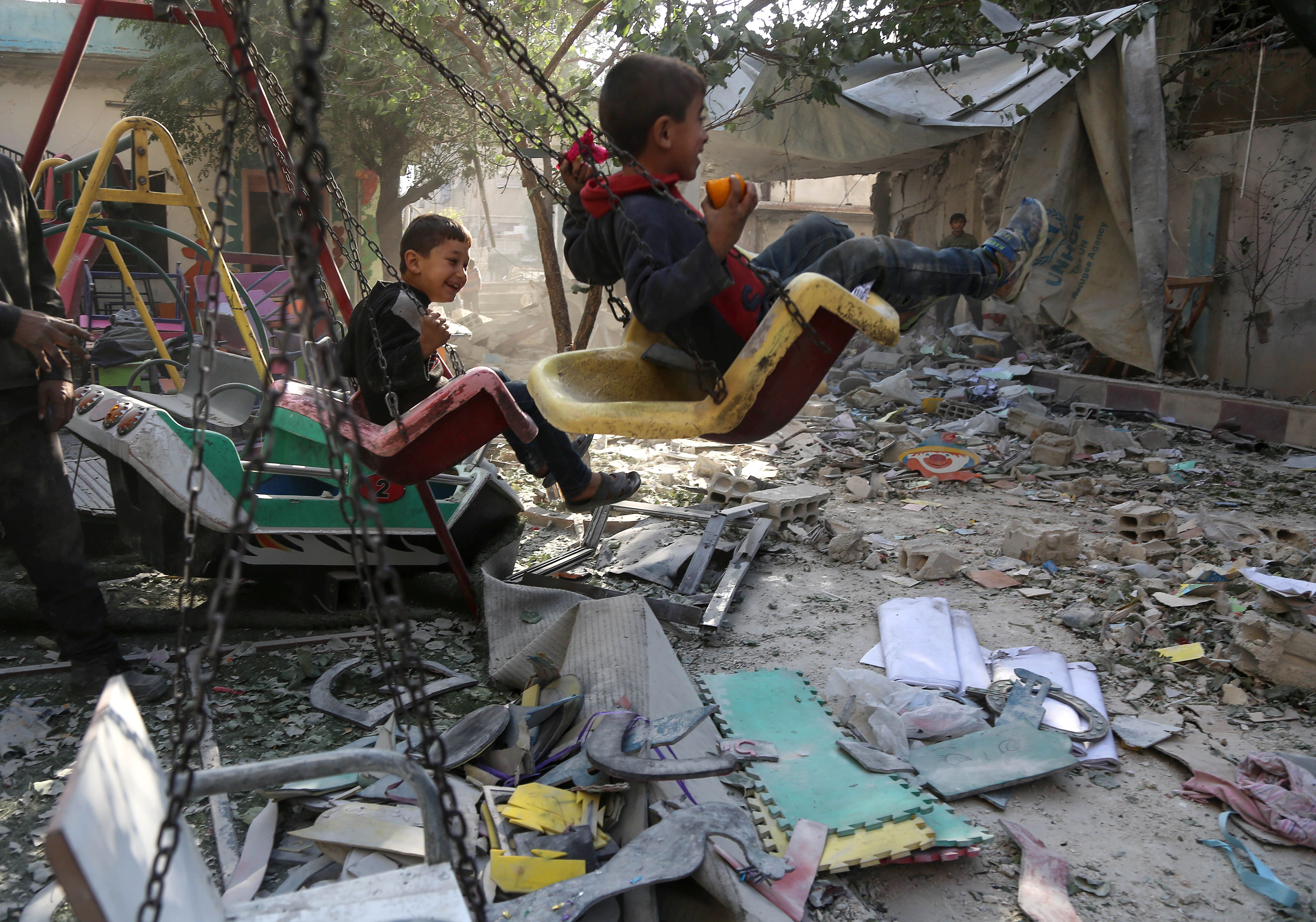 Syrian boys swing on the playground outside their damaged school on November 9th, 2017, in the besieged rebel-held Eastern Ghouta town of Hamouriyah, following air raids by government forces the previous day.