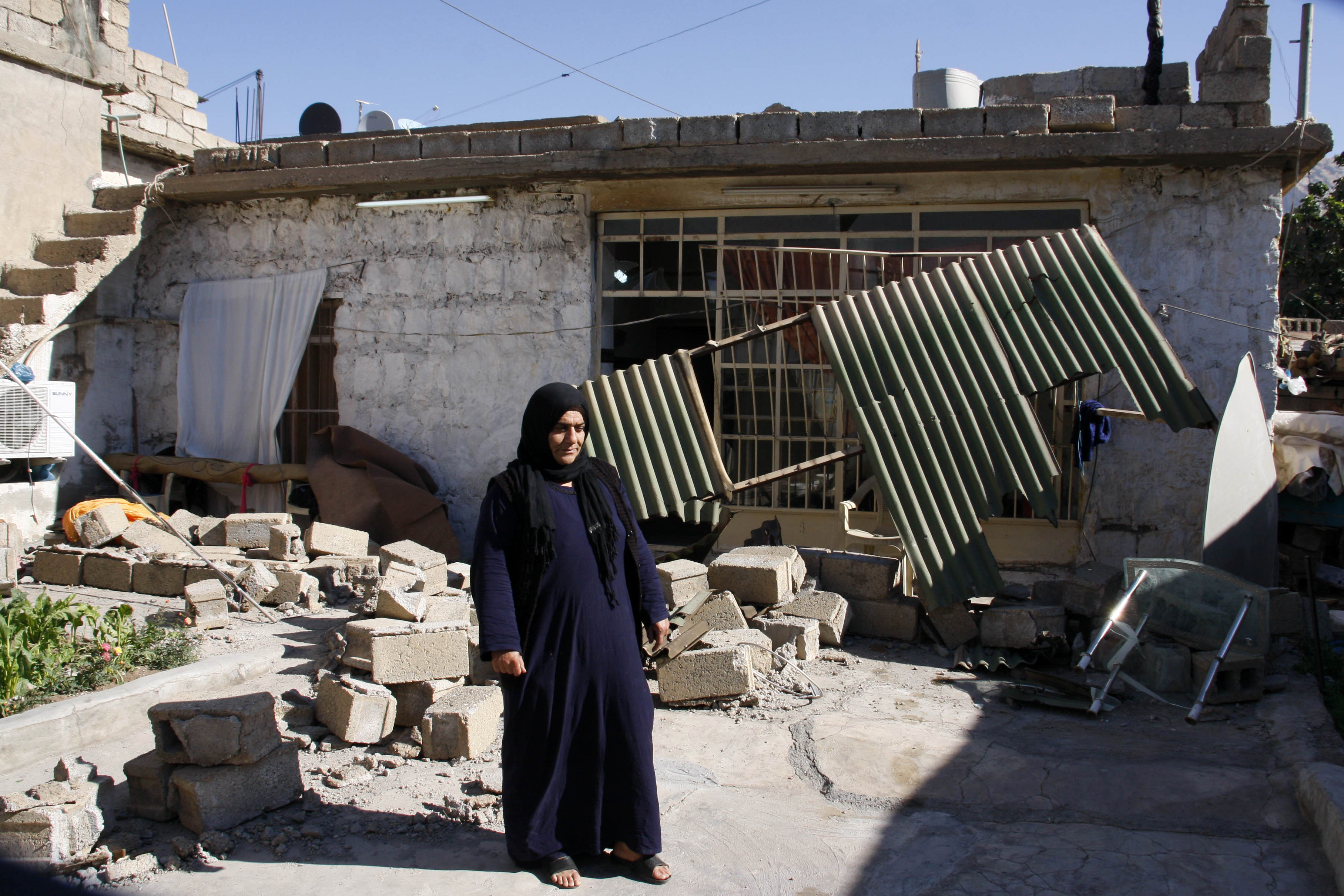 A woman stands in the yard next to her damaged home in the mountainous town of Darbandikhan in Iraqi Kurdistan on November 13th, 2017.