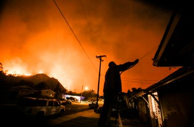 A man waters his home as firefighters battle the Thomas fire along a hillside near homes in Santa Paula, California, on December 5th, 2017.