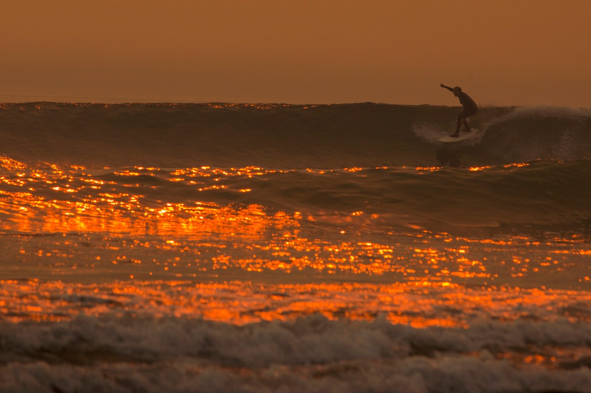 A smoke-filled sky filters orange light around a surfer as the Thomas Fire continues to grow and threaten communities from Carpinteria to Santa Barbara on December 12th, 2017, in Carpinteria, California.