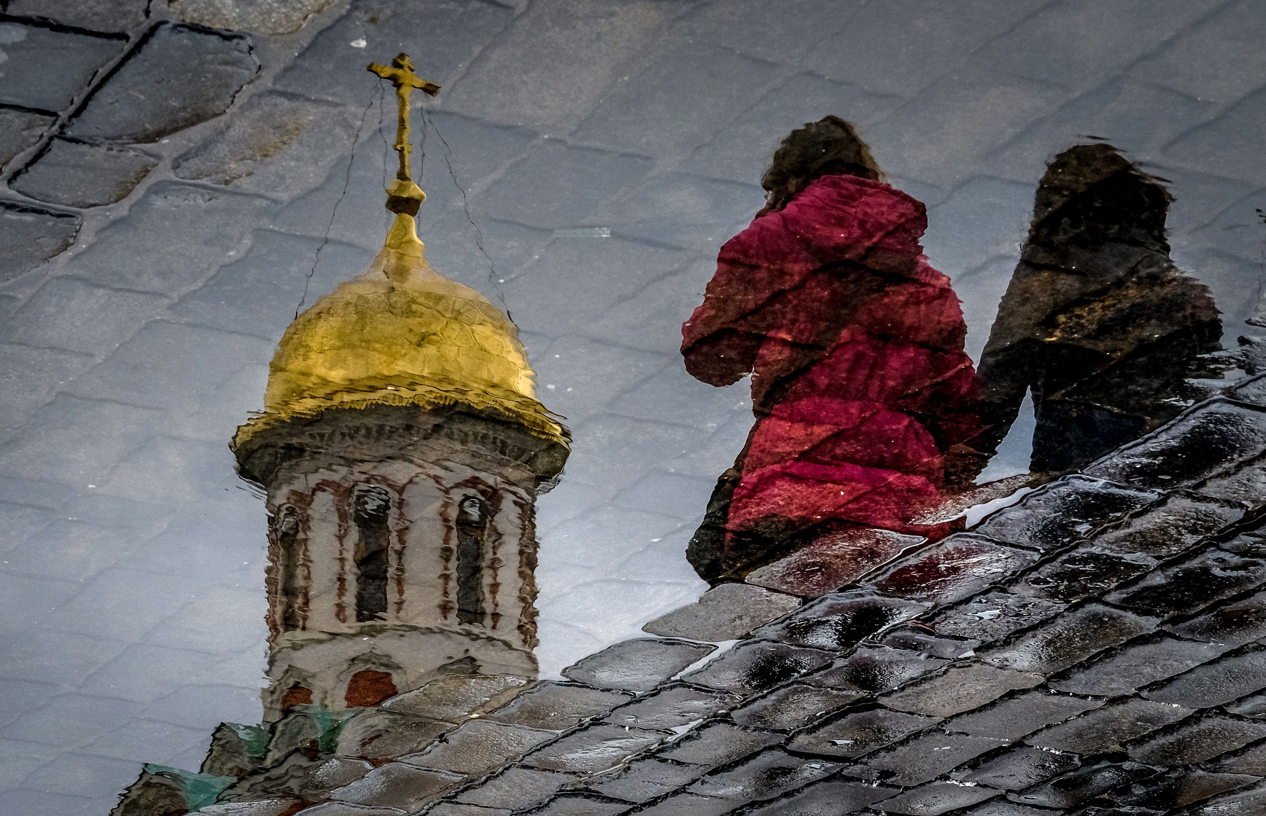 Women are reflected in a puddle as they walk across the Red Square in Moscow on April 26th, 2018.