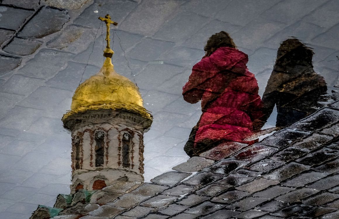 Women are reflected in a puddle as they walk across the Red Square in Moscow on April 26th, 2018.