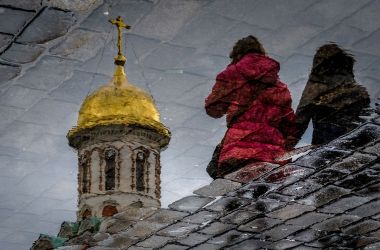 Women are reflected in a puddle as they walk across the Red Square in Moscow on April 26th, 2018.