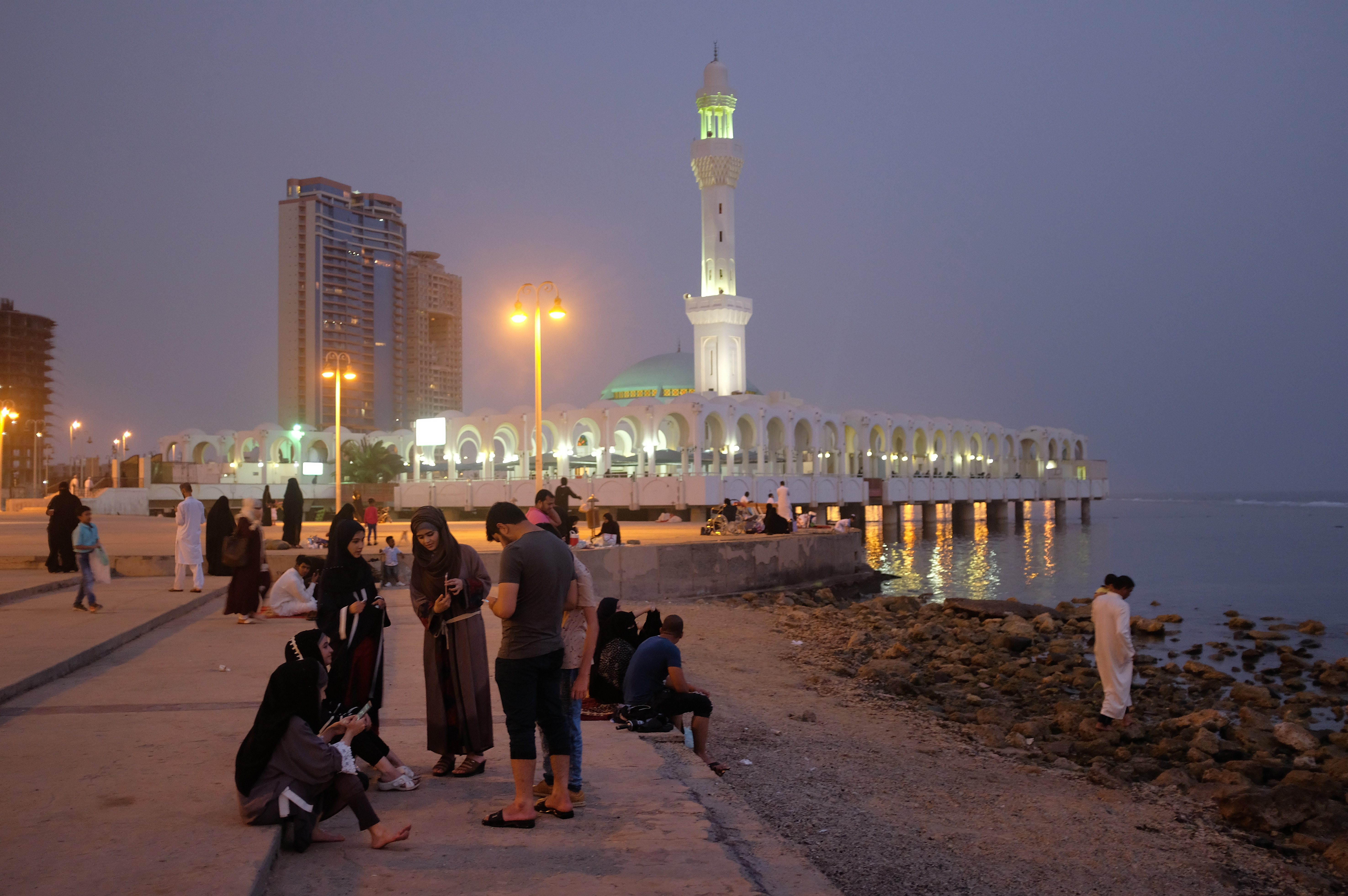 People relax on a Friday evening along the Corniche waterfront as the Al Rahma mosque stands behind on June 22nd, 2018, in Jeddah.