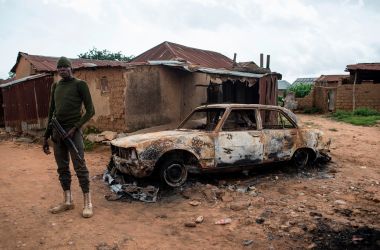 A member of the security forces stands next to a burnt vehicle in the Nghar Village, near Jos, on June 27th, 2018, after Fulani herdsmen attacked the village. Plateau State in Nigeria has seen days of violence where more than 200 people have been killed in clashes between Berom farmers and Fulani herders. Nigeria is facing an escalation in clashes between farmers and herders over land use and resources that is deepening along religious and ethnic lines.