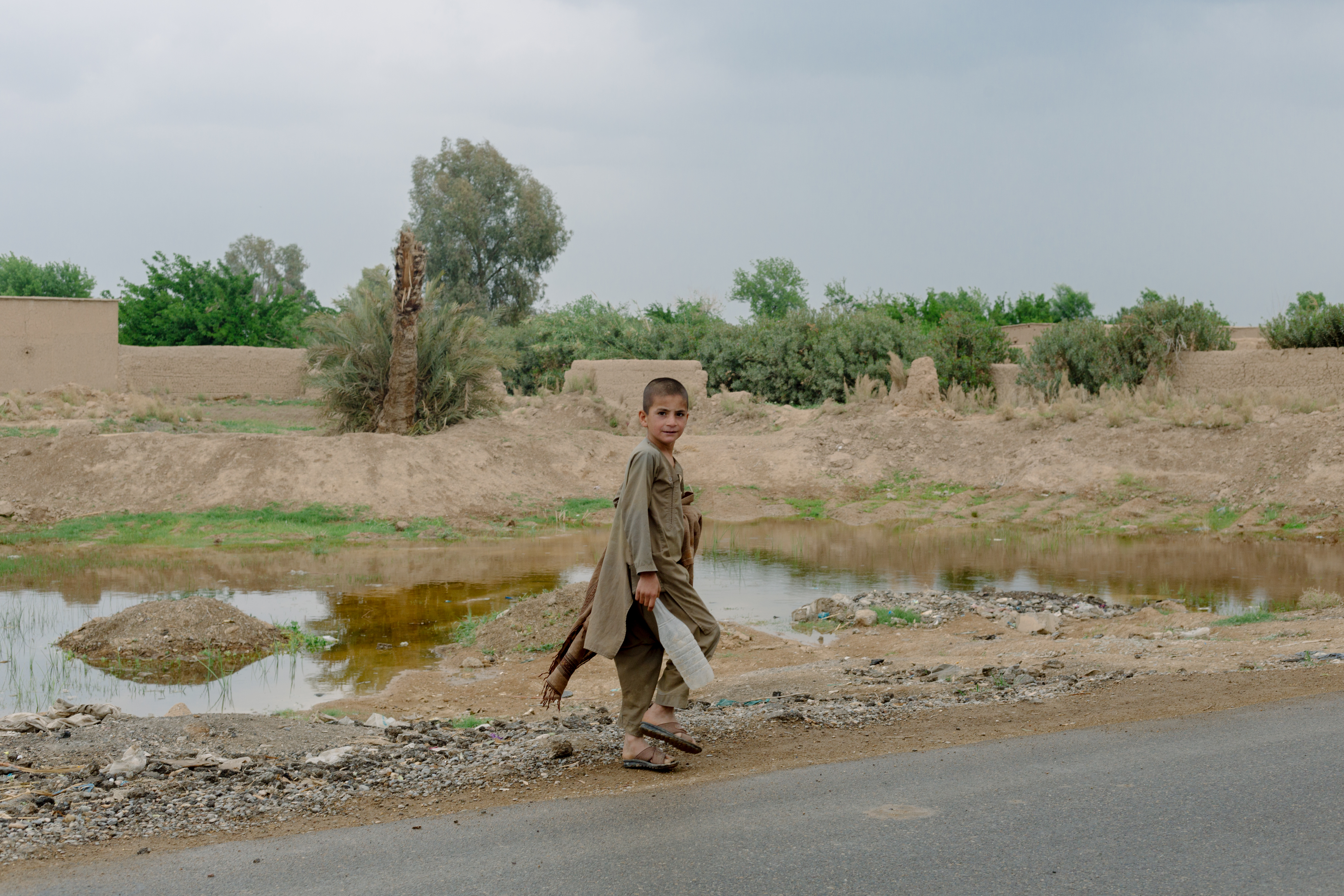 In April of 2019, a boy walks past a small pond formed by a single U.S. bomb dropped during heavy fighting to retake Nad Ali, two years earlier.