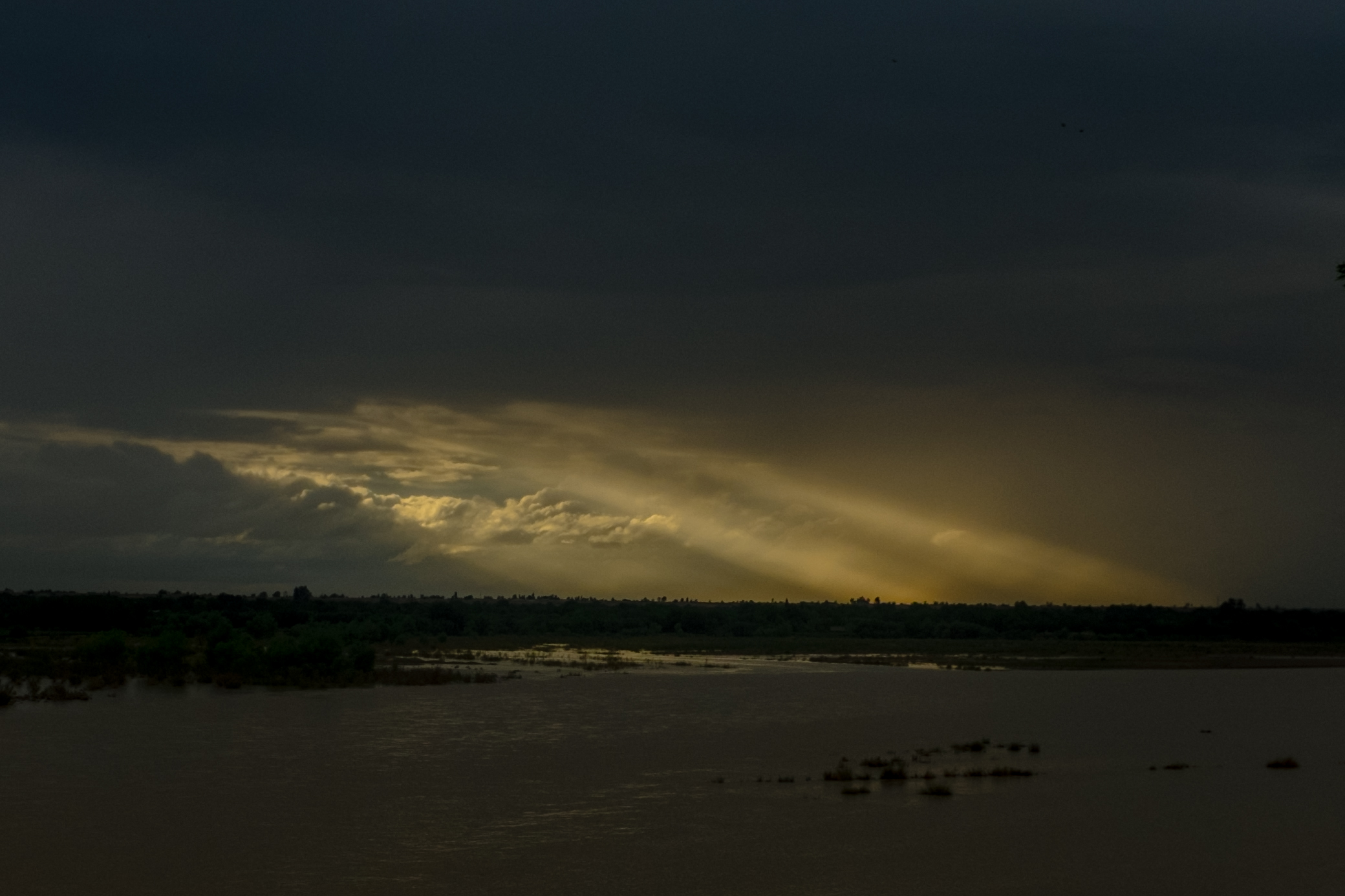 Across the overflowing Helmand River from Lashkar Gah, sunlight breaks through the clouds over Nad Ali in April of 2019.