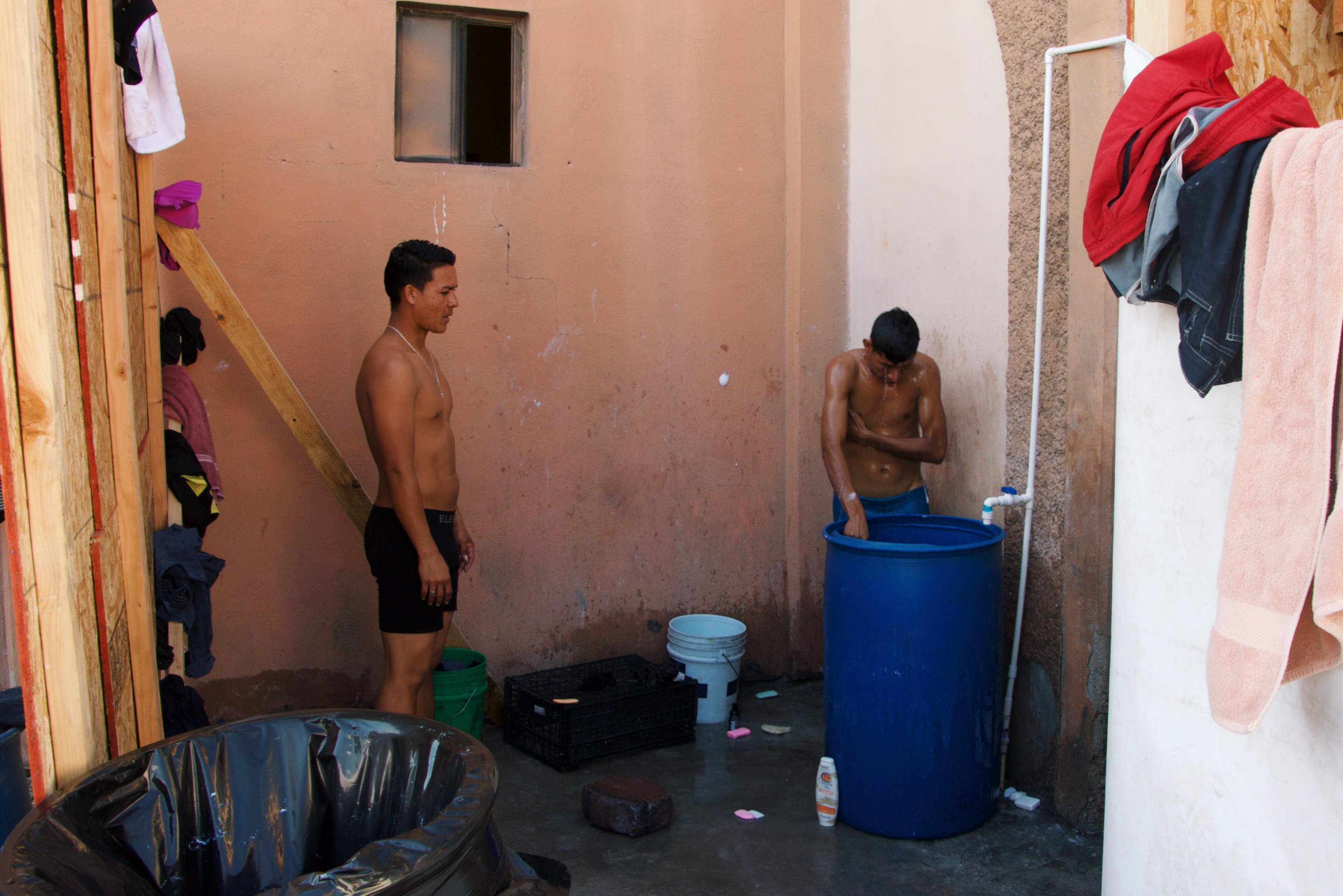 Two migrants wash in the rudimentary bathing area inside the pavilion for children and families.