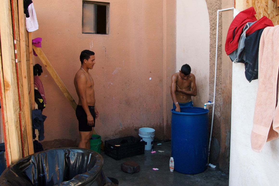 Two migrants wash in the rudimentary bathing area inside the pavilion for children and families.