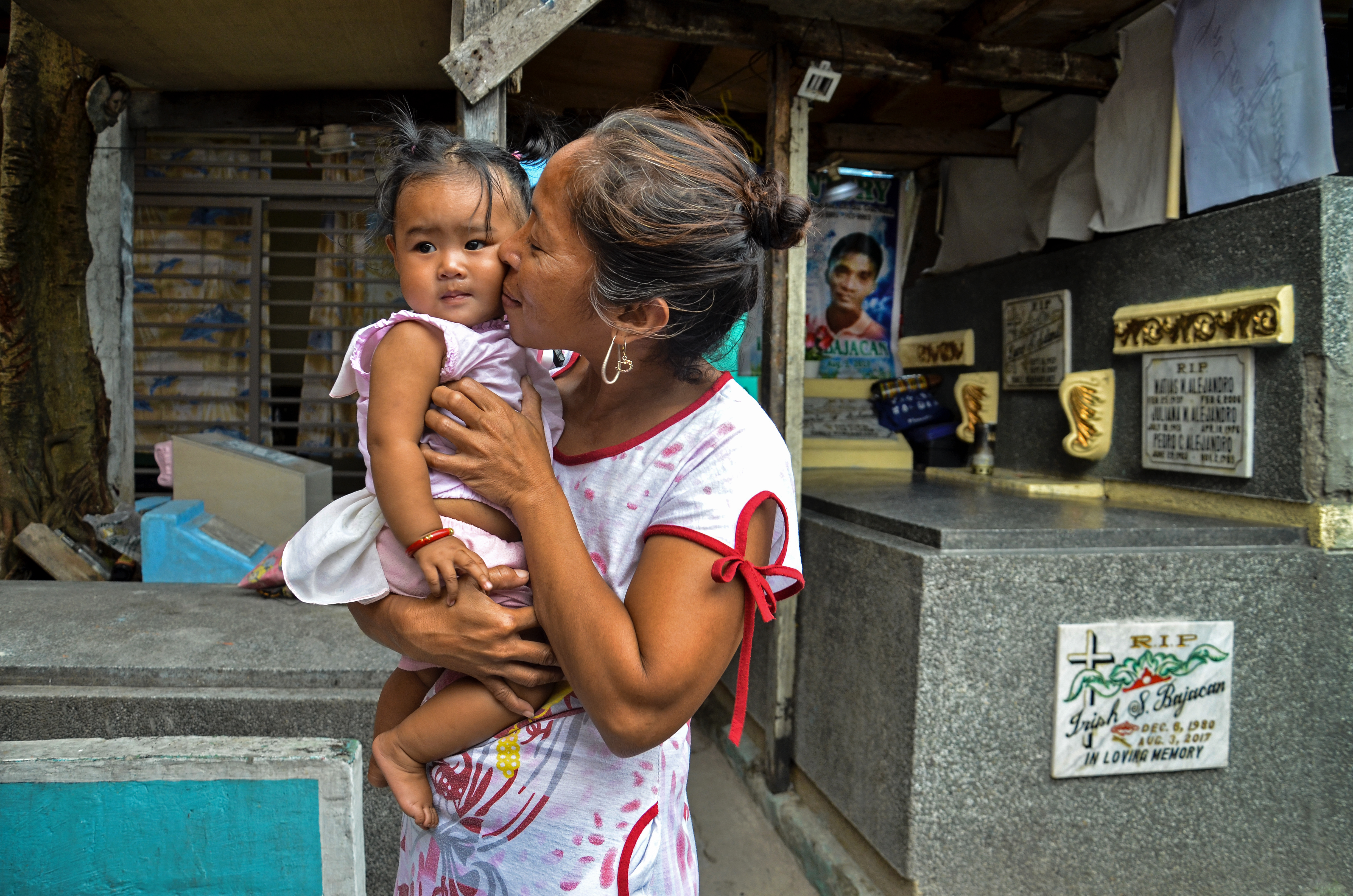 Irish's wife and youngest daughter stand in front of his grave, which lies underneath the family home in Manila North Cemetery. His funeral banner still hangs above the grave.