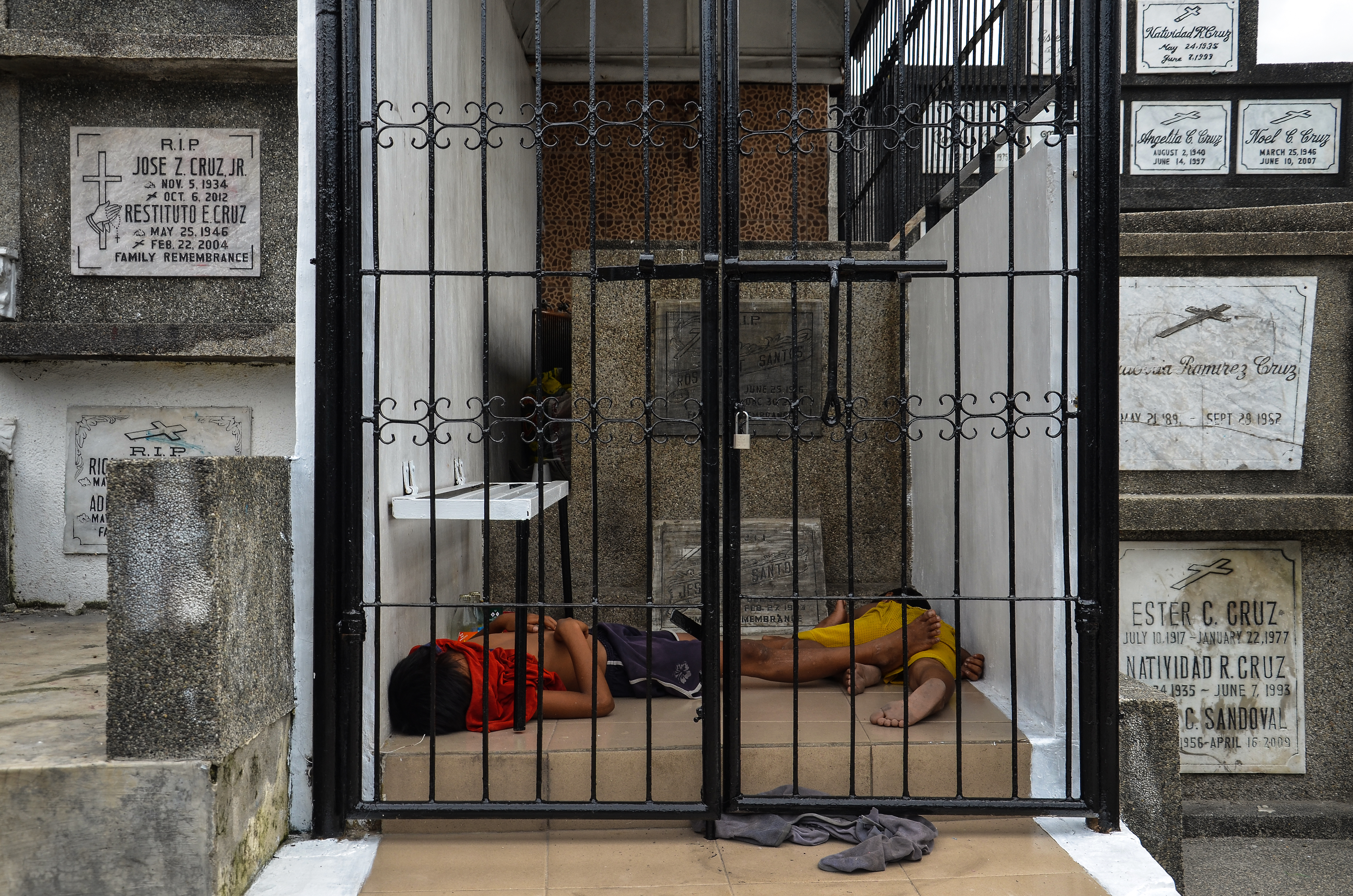 Two boys sleep in the heat of the day in a mausoleum, where their father is a caretaker, in Manila North Cemetery.