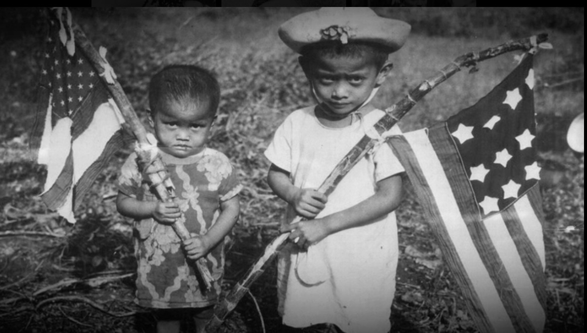 Chamarro children welcome U.S. troops during World War II with homemade flags.