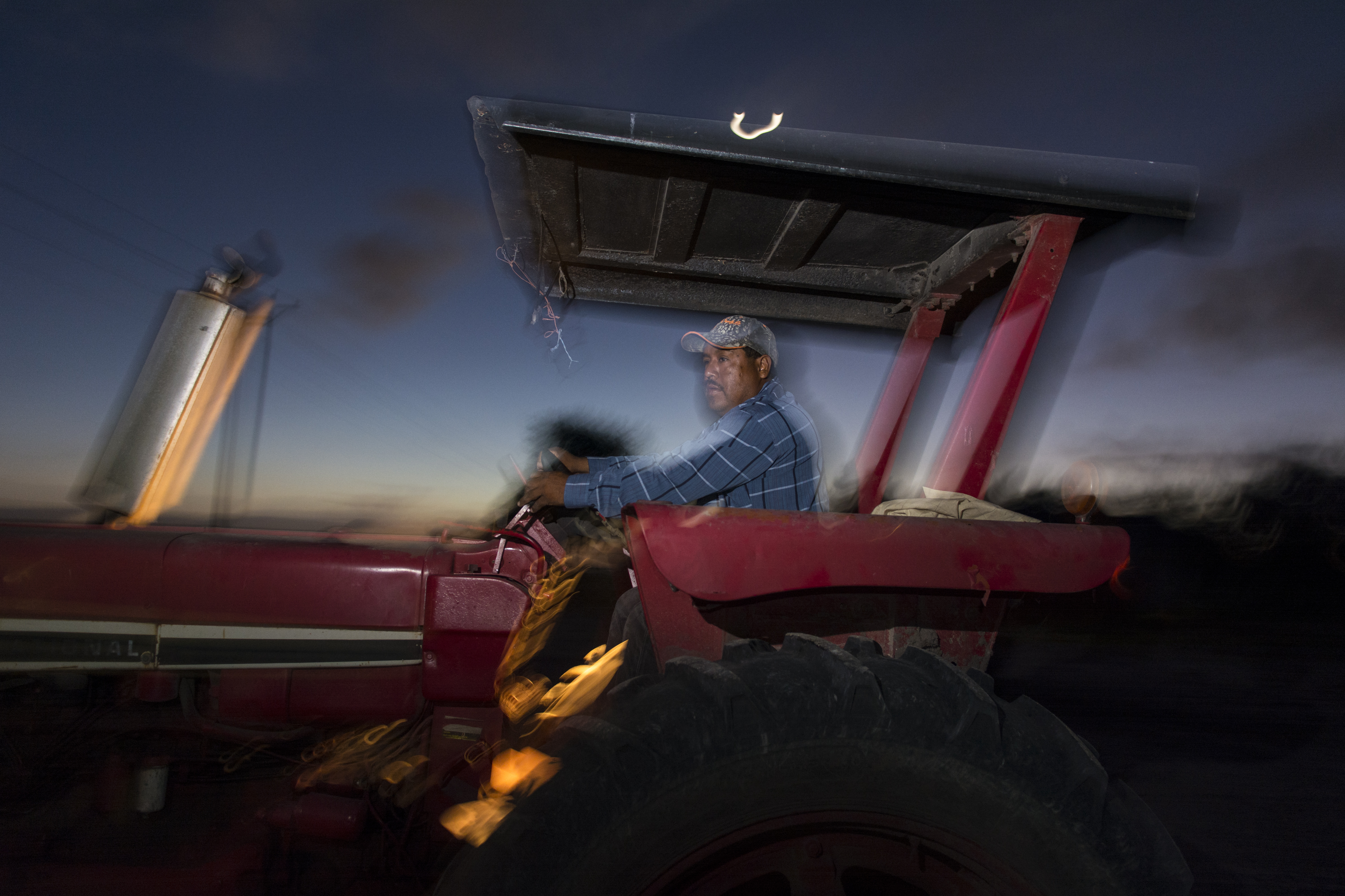 Before dawn, a man boards and starts the tractor he will drive all day in the sugarcane fields of South Texas.