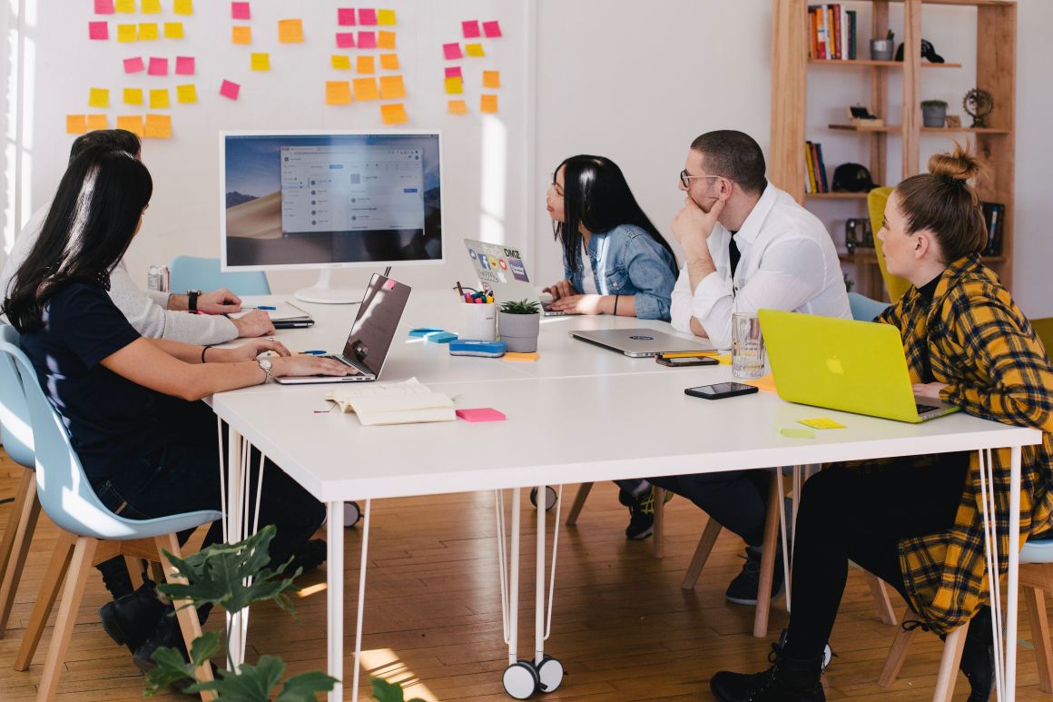 A group of coworkers has a meeting in a tech office.