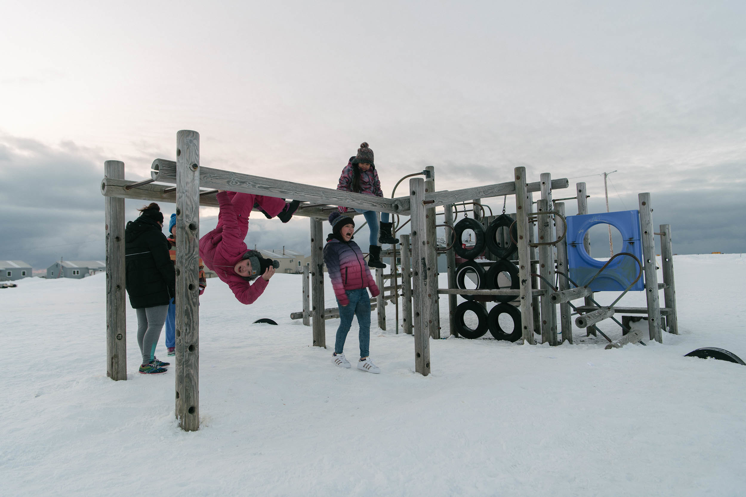 Kids play on a snowy playground in the light of Arctic spring. With each new generation, the traumas experienced by previous generations grow more distant, though the community's youth will undoubtedly face new challenges as they come of age.